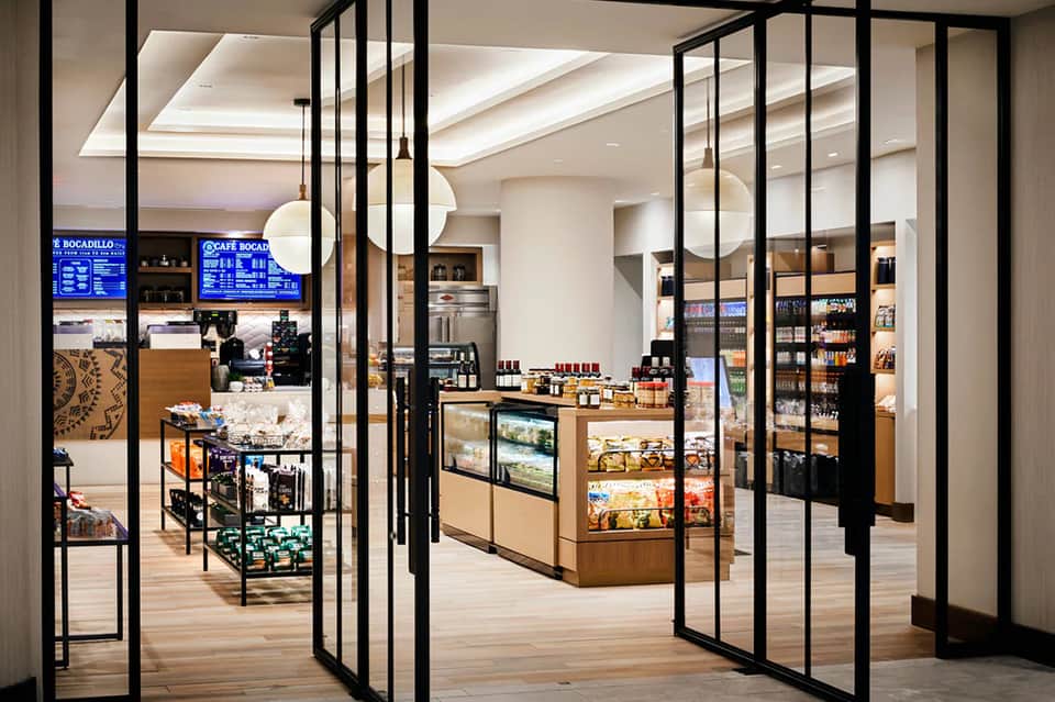 Modern café interior with black-framed glass doors, wooden counters, shelving, and blue menu displays