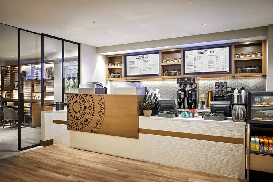 Modern coffee shop counter with wooden accents, menu boards, espresso machine, and geometric patterned décor