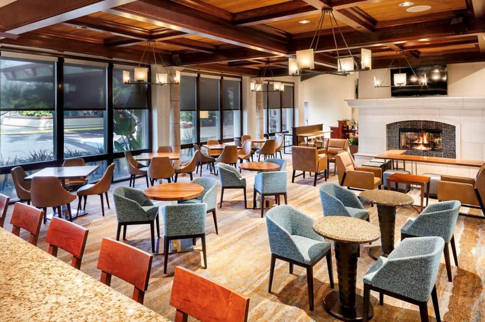 Upscale hotel lounge with wooden ceiling beams, fireplace, and mixed seating including blue chairs and wooden tables