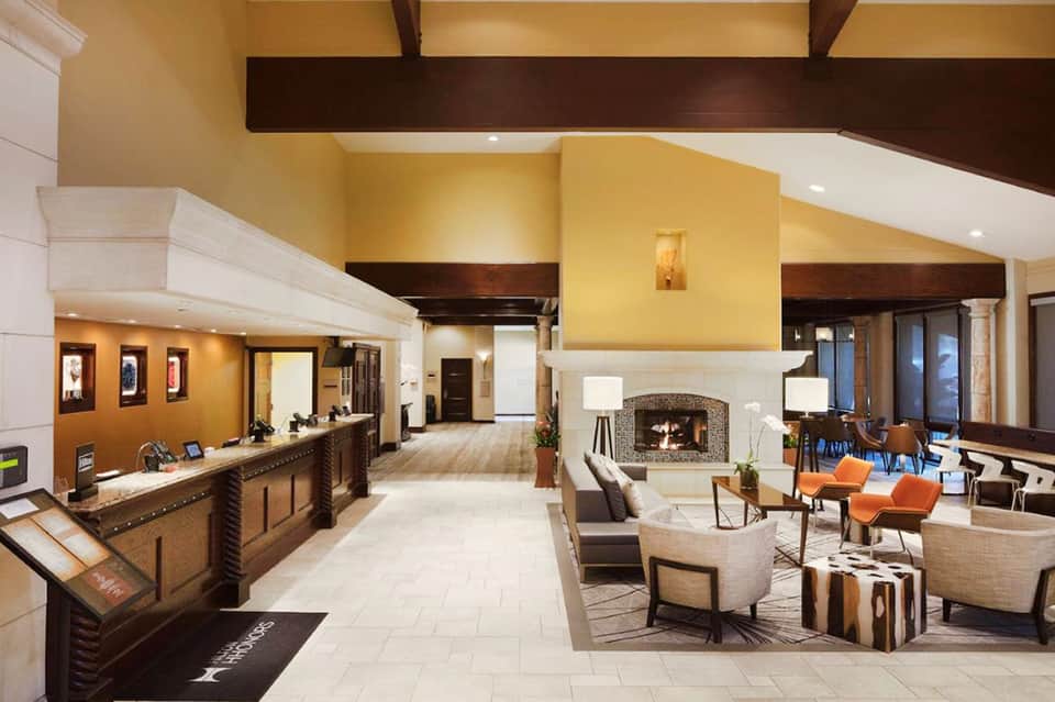 Spacious hotel lobby with yellow walls, dark wood beams, fireplace, reception desk, and comfortable seating areas