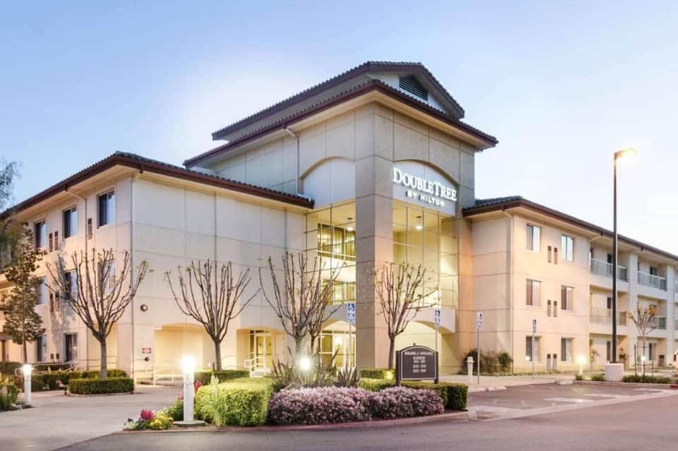 DoubleTree by Hilton hotel exterior with cream-colored facade, dark roof, and manicured purple flowering bushes