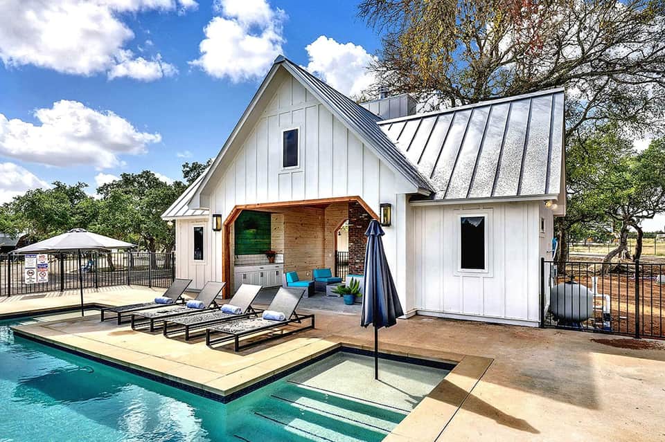 Modern white farmhouse with pool, lounge chairs, and covered patio area