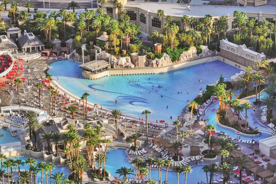 Aerial view of large resort with multiple blue pools, palm trees, and recreational water features