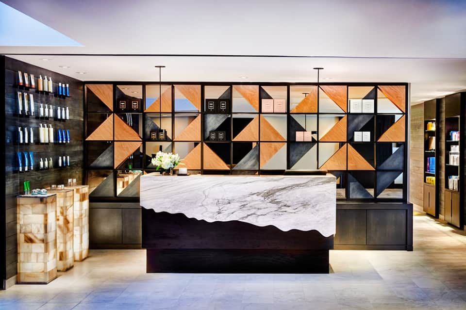 Luxury spa reception desk with geometric patterned storage wall in black, orange, and natural wood tones