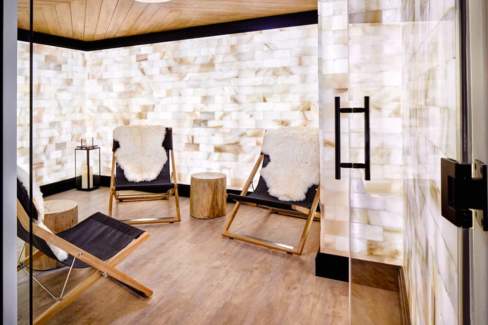 Spa relaxation room with cream chairs, white stone walls, wooden ceiling, and minimalist décor