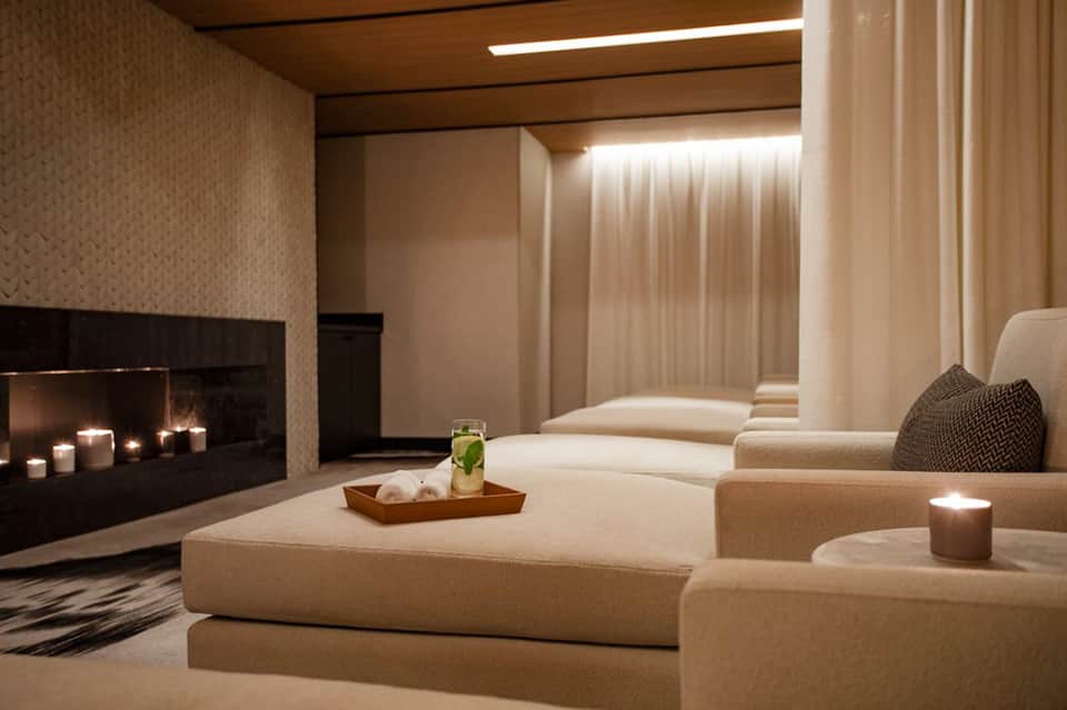 Luxury spa lounge with cream sectional sofa, fireplace with candles, and sheer curtains