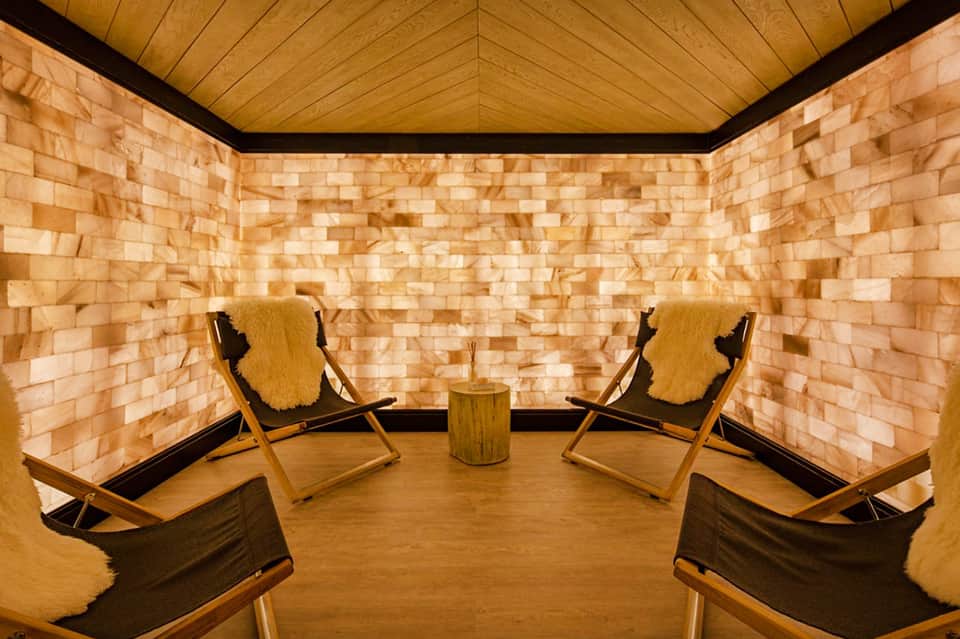 Spa relaxation room with salt brick walls, wooden ceiling, two lounge chairs with fur throws, and central side table