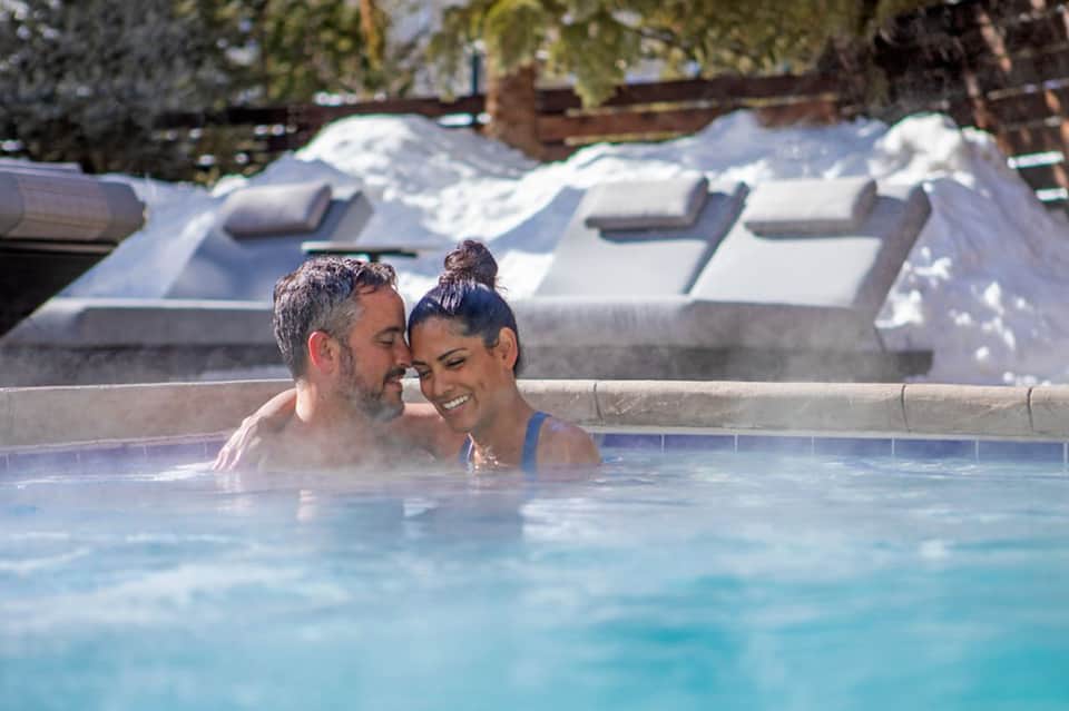 Couple enjoying hot spring thermal pool with snow-covered roofs in background