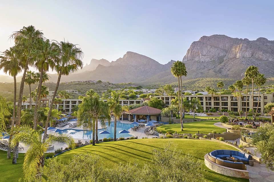 Luxury resort courtyard with pool, palm trees, and dramatic mountain backdrop