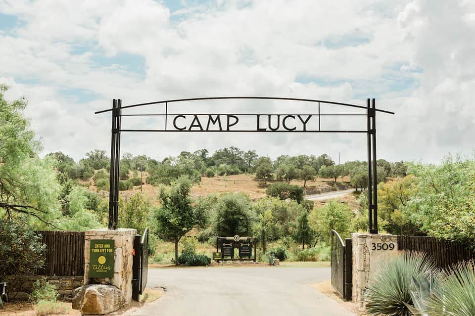 Camp Lucy entrance gate with rustic metal arch and pastoral landscape view
