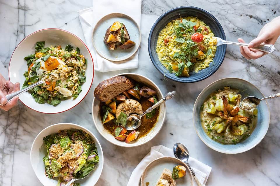 Overhead view of multiple colorful bowls with grain dishes, eggs, and roasted vegetables on marble table