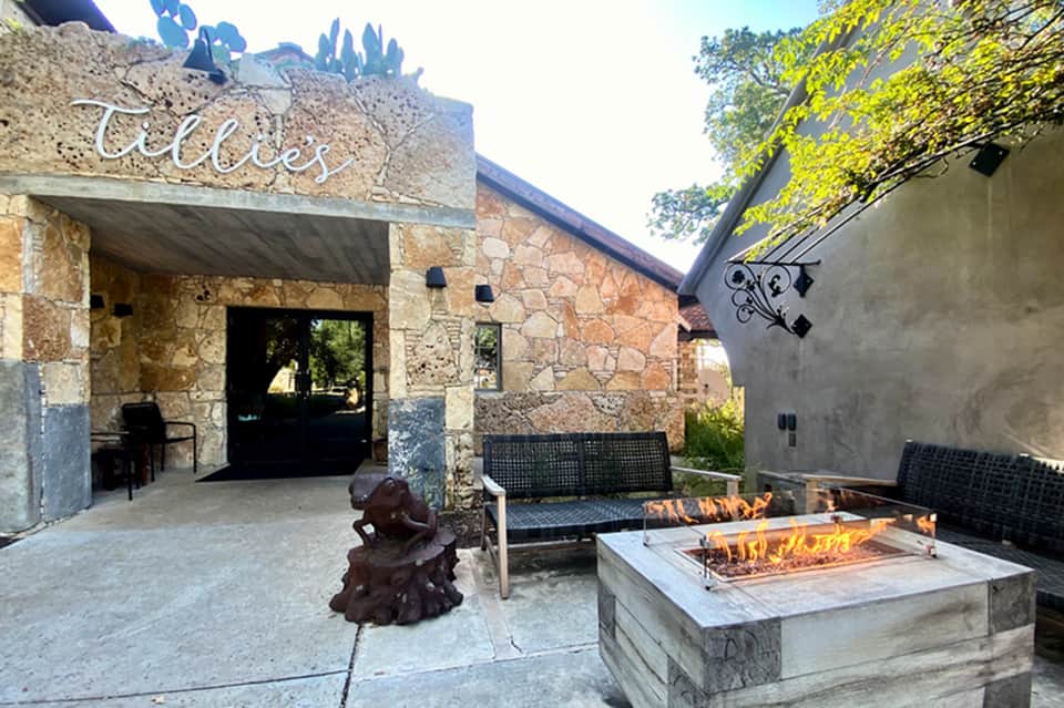 Outdoor patio with fire pit, stone building labeled 'Collies', and seating areas surrounded by greenery