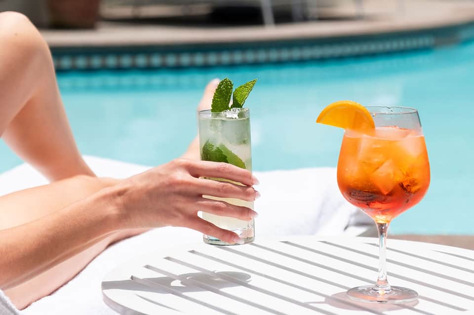 Guest holding mojito by pool with colorful cocktail nearby