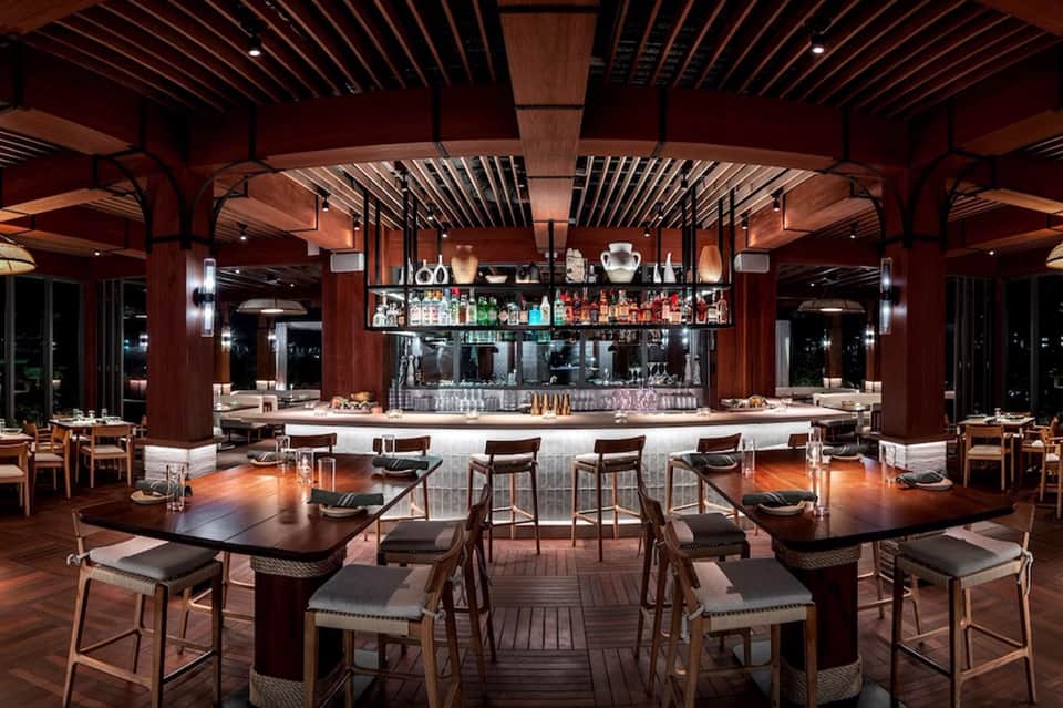 Upscale restaurant with wood ceiling, central bar, and dining tables with leather chairs