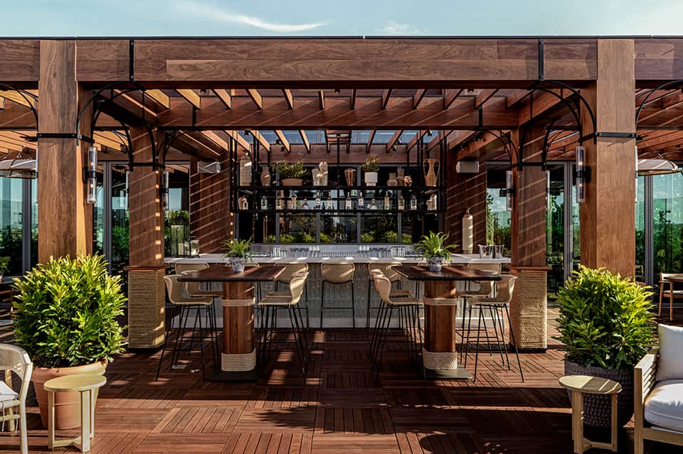 Outdoor rooftop bar with wooden pergola, terrace seating, and mountain views