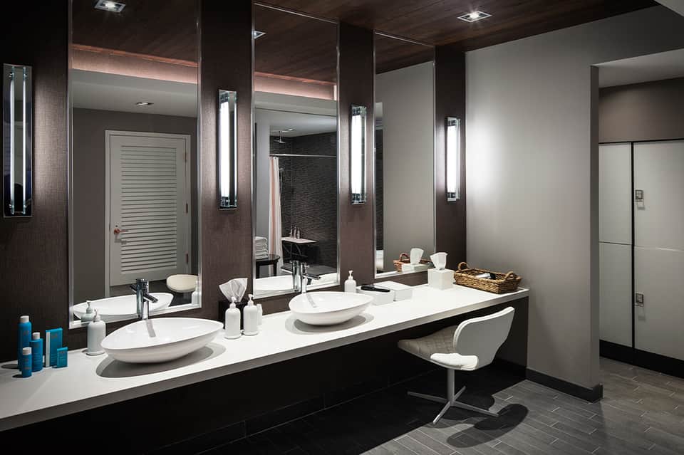 Luxury bathroom with dual vanities, large mirrors, illuminated sconces, and dark wood accent walls