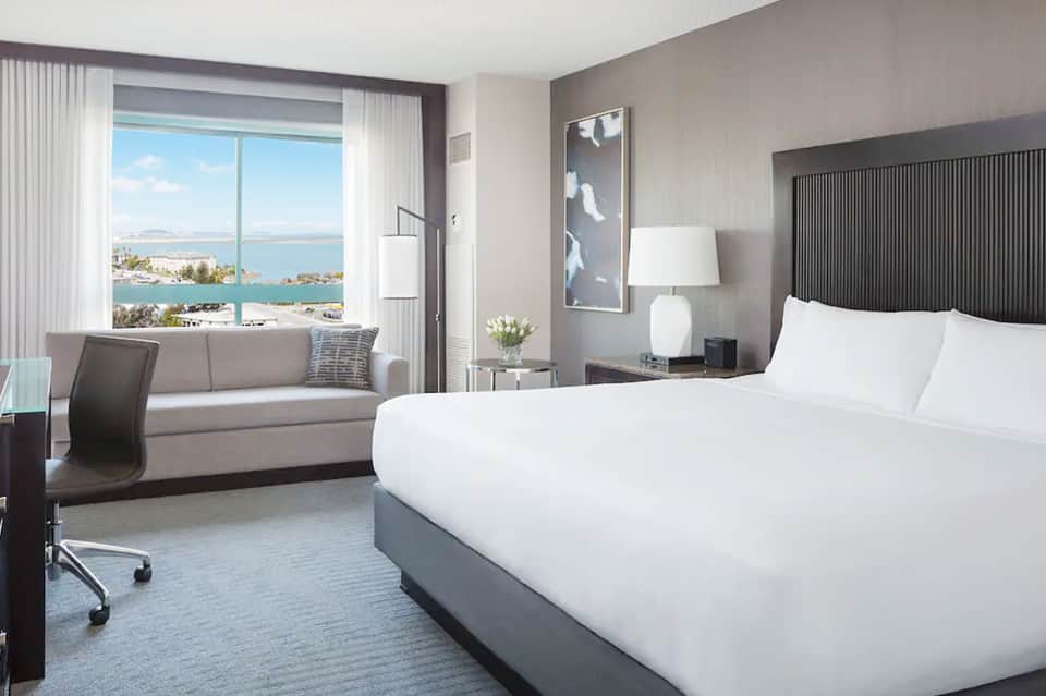 Luxury hotel room with floor-to-ceiling windows overlooking a bay and coastal cityscape