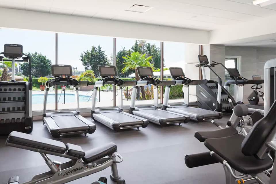 Modern fitness center with cardio equipment and large windows overlooking outdoor pool and landscaping
