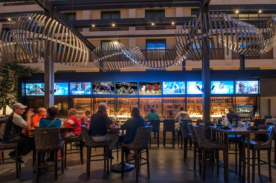 Modern outdoor bar with curved metal structures and blue lighting overlooking a city courtyard
