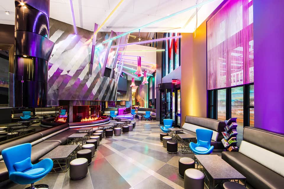 Modern hotel lounge with vibrant purple lighting, neon accents, blue chairs, and fireplace seating area