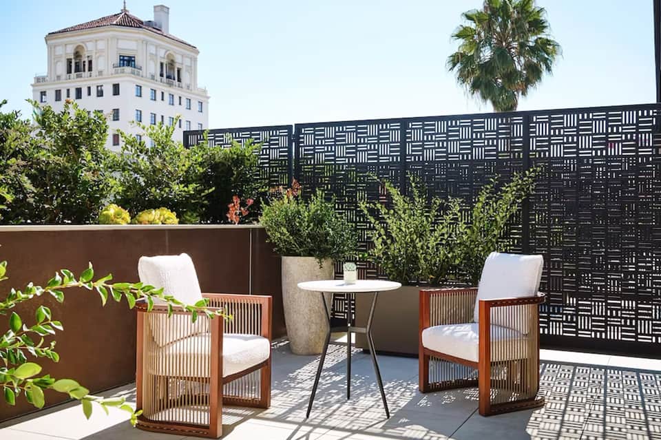 Modern rooftop terrace with wooden chairs, geometric black privacy screen, potted plants, and historic building in background