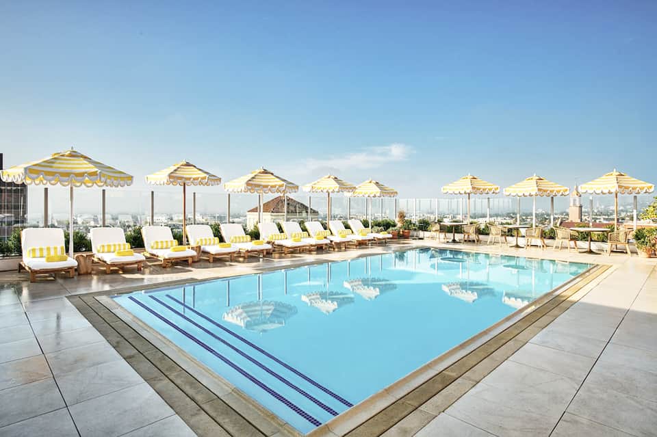 Rooftop pool with yellow striped umbrellas, lounge chairs, and city skyline views