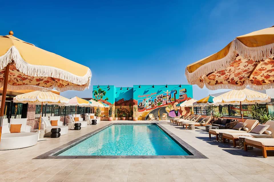 Retro-styled resort pool with yellow umbrellas, lounge chairs, and vintage signage under clear blue sky