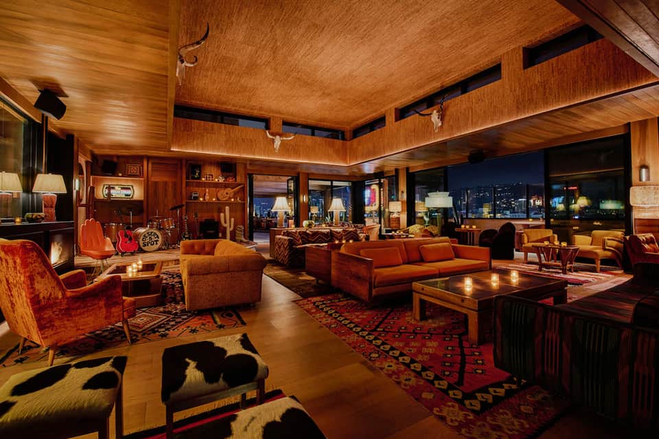 Luxury penthouse lounge with wood ceilings, orange seating, ornate rugs, fireplace, and city skyline views