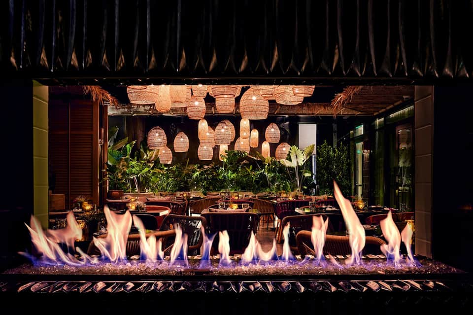 Elegant outdoor dining area with fire pit, hanging lanterns, and lush greenery at night