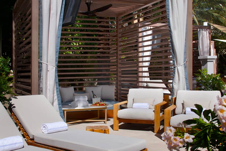 Outdoor lounge area with wooden pergola, cream cushioned seating, and lush tropical plants