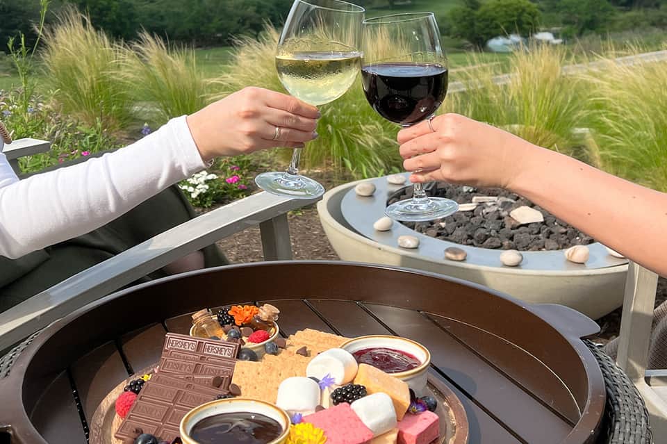 Two people toasting wine glasses at an outdoor garden venue with chocolate fondue and berries
