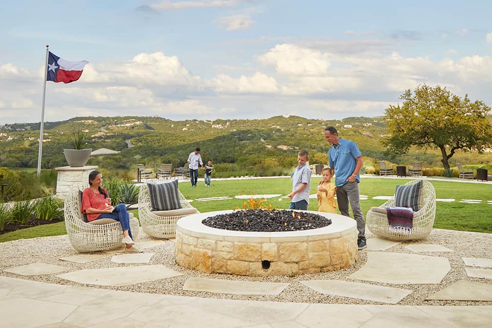 Outdoor fire pit area with stone seating and Texas flag overlooking green hills and valley landscape