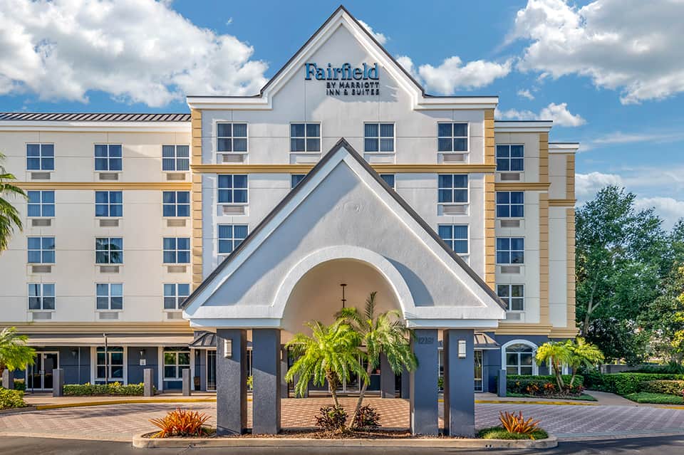Fairfield by Marriott Inn & Suites hotel exterior with white facade, arched entrance, and palm tree landscaping