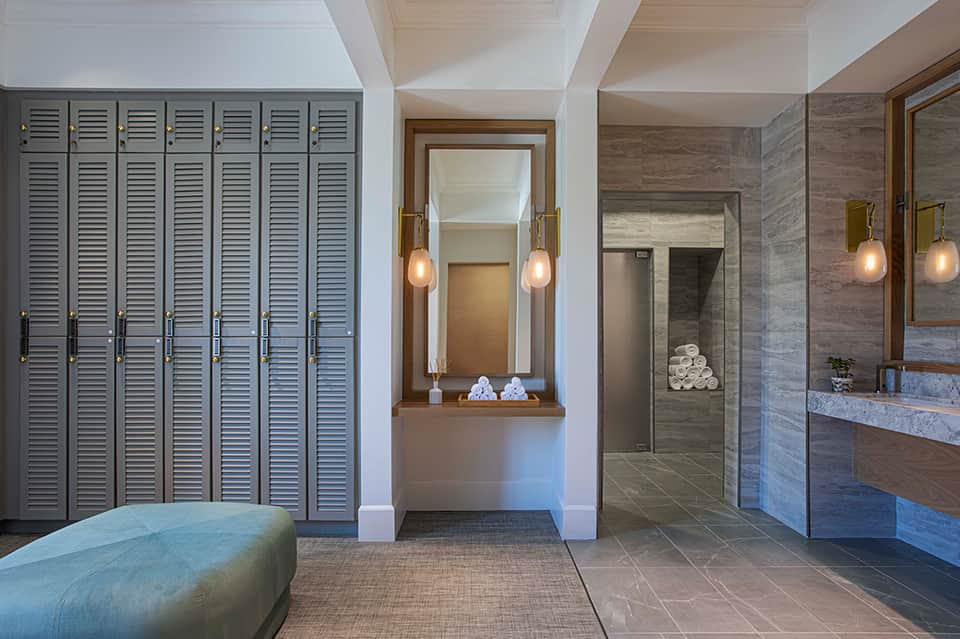 Luxury spa locker room with wooden lockers, vanity mirrors, pendant lighting, and access to shower area