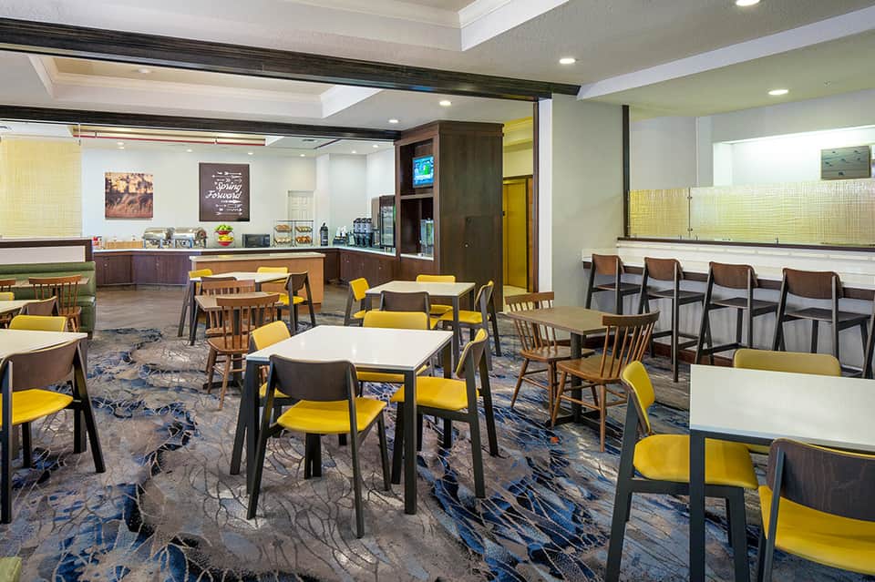 Casual dining area with yellow chairs, white tables, and modern wood accents in a bright hotel breakfast room