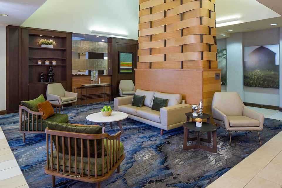 Modern hotel lobby with wooden column, beige seating, blue patterned rug, and dark wood shelving