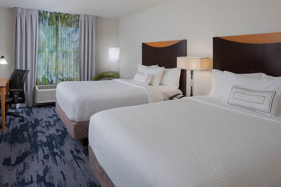 Modern hotel room with two queen beds, dark headboards, white bedding, and large windows with nature views