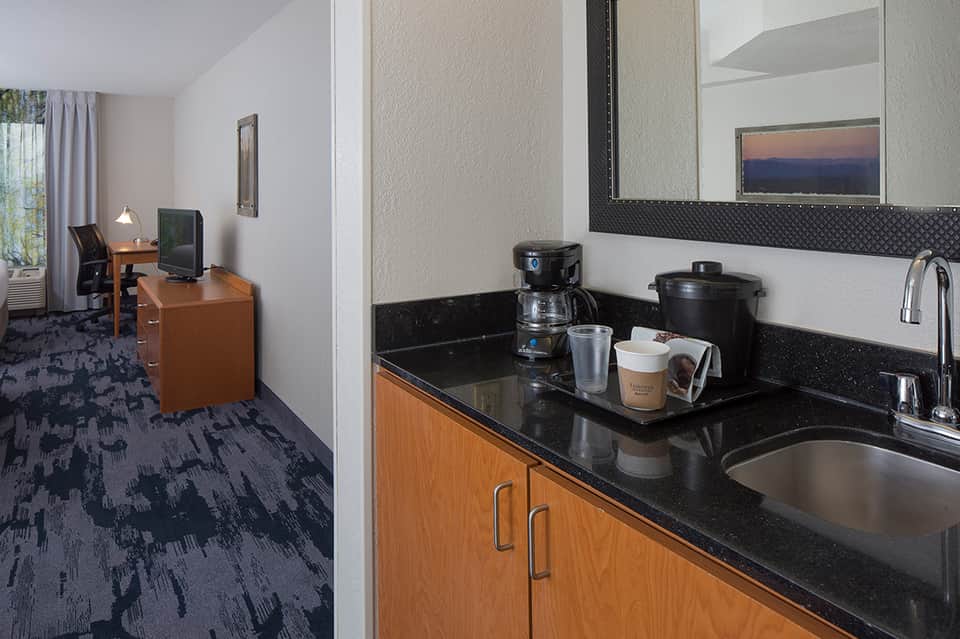 Hotel room kitchenette with black granite countertop, wood cabinets, and sink, with workspace visible in background