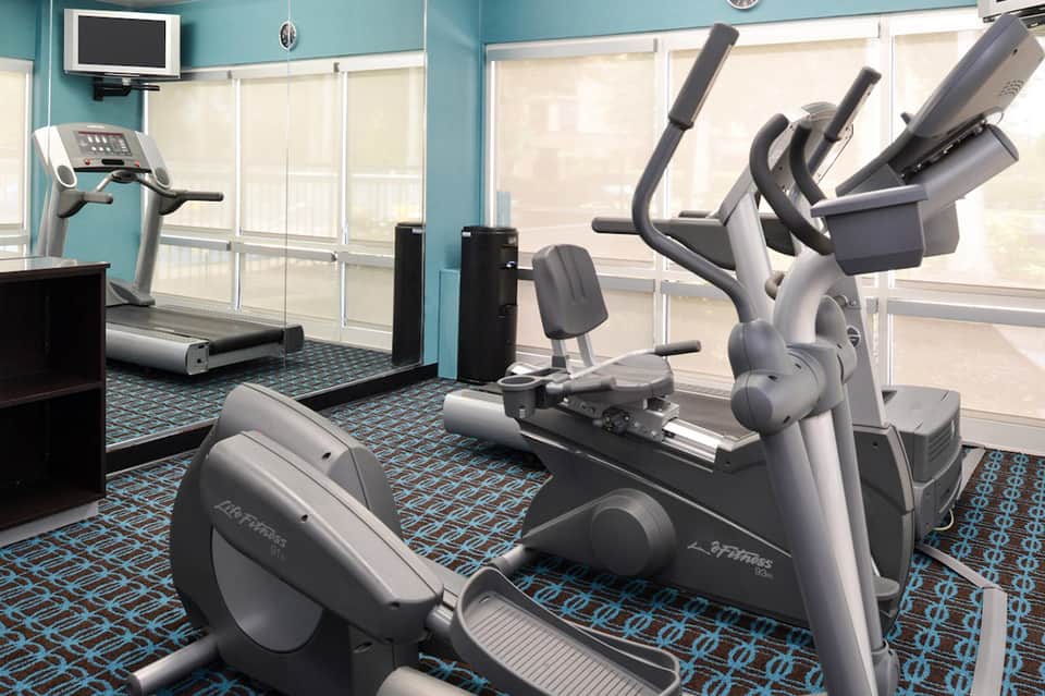 Modern fitness center with cardio equipment, stationary bikes, and treadmill overlooking windows with turquoise walls