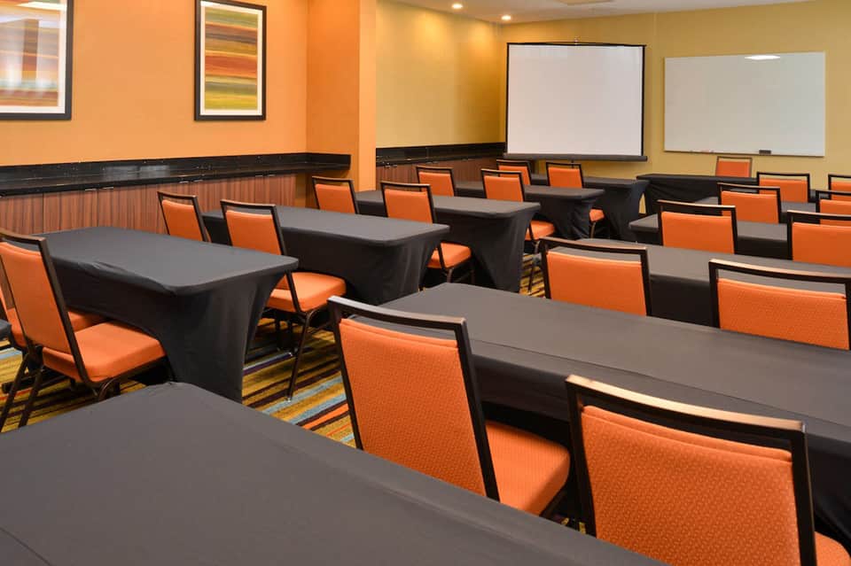 Modern conference room with orange chairs, black tables with black table skirts, and presentation screens on walls