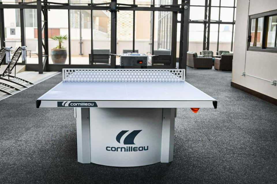 Cornilleau white ping pong table in modern indoor recreation room with floor-to-ceiling windows