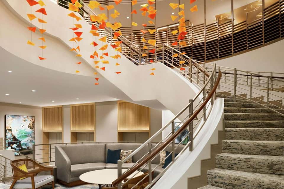 Modern hotel atrium with hanging orange paper decorations, curved staircase, and contemporary seating area