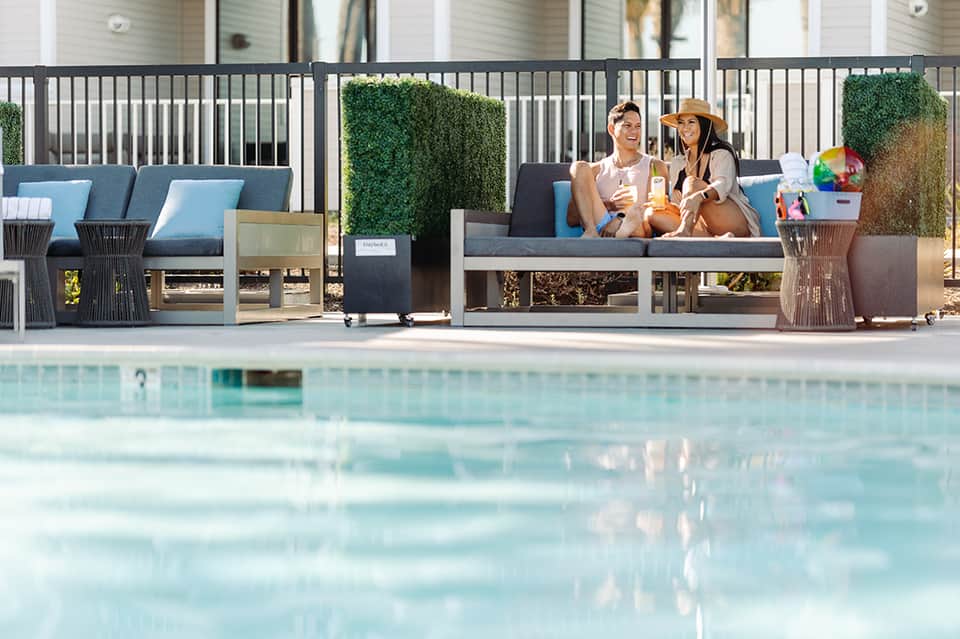 Resort poolside lounge area with guests relaxing on blue cushioned seating near modern white railings