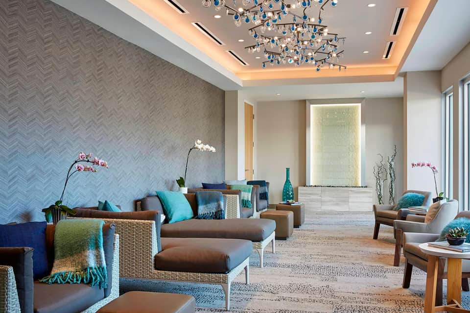 Elegant lounge with turquoise accents, brown furniture, herringbone wallpaper, and modern chandelier