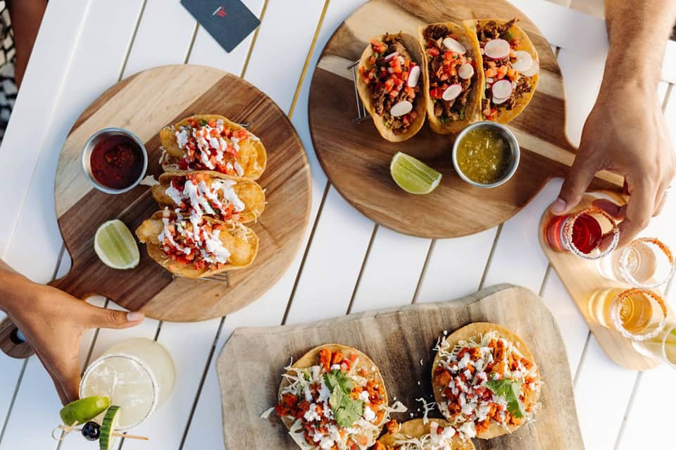 Three wooden boards with gourmet tacos topped with white cheese and fresh vegetables, served with lime and salsa