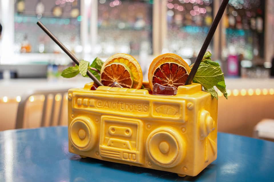 Yellow boombox-shaped cocktail glass with orange citrus slices and mint garnish on blue table