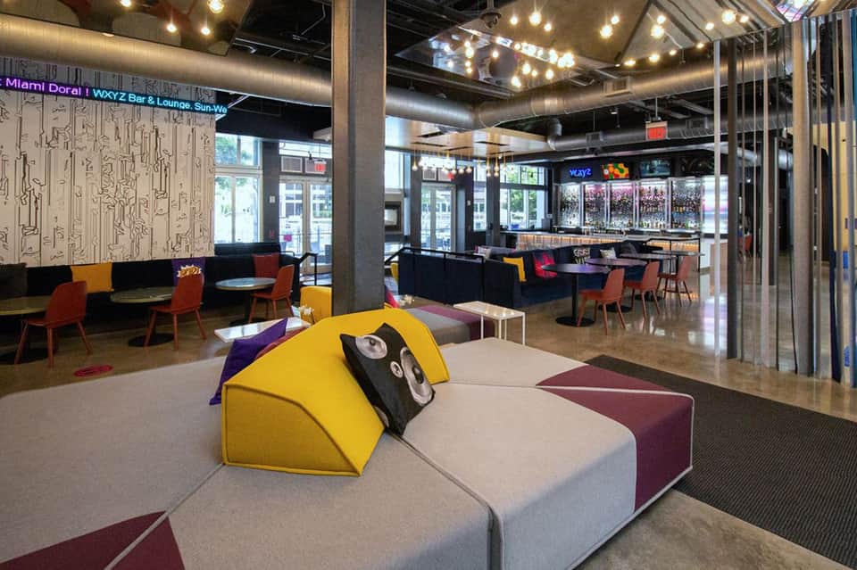 Modern hotel lobby with colorful modular seating, yellow and burgundy chairs, and interactive wall art