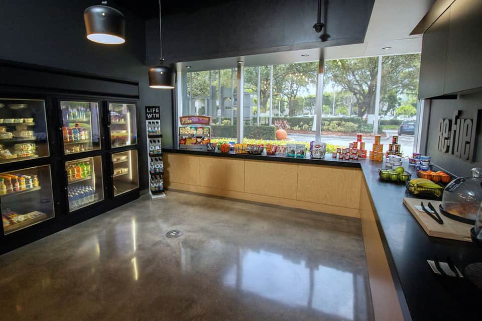 Modern hotel snack bar with refrigerated displays, counter service area, and large windows overlooking landscaped grounds