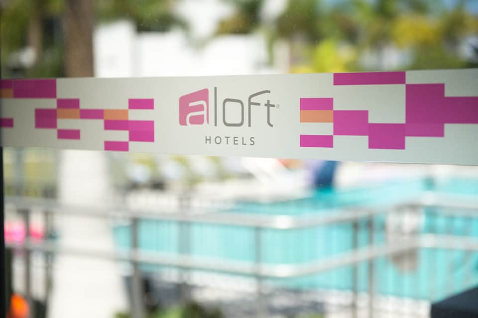Aloft Hotels logo on glass window with blurred pool and resort background