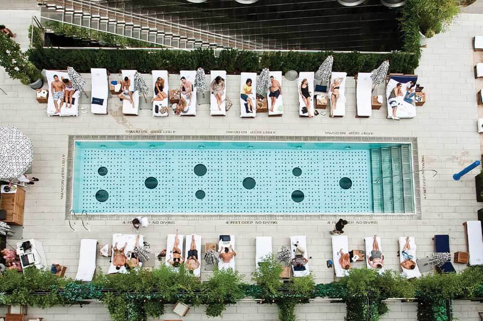 Aerial view of resort pool with swimmers on lounge chairs along the deck and green landscaping